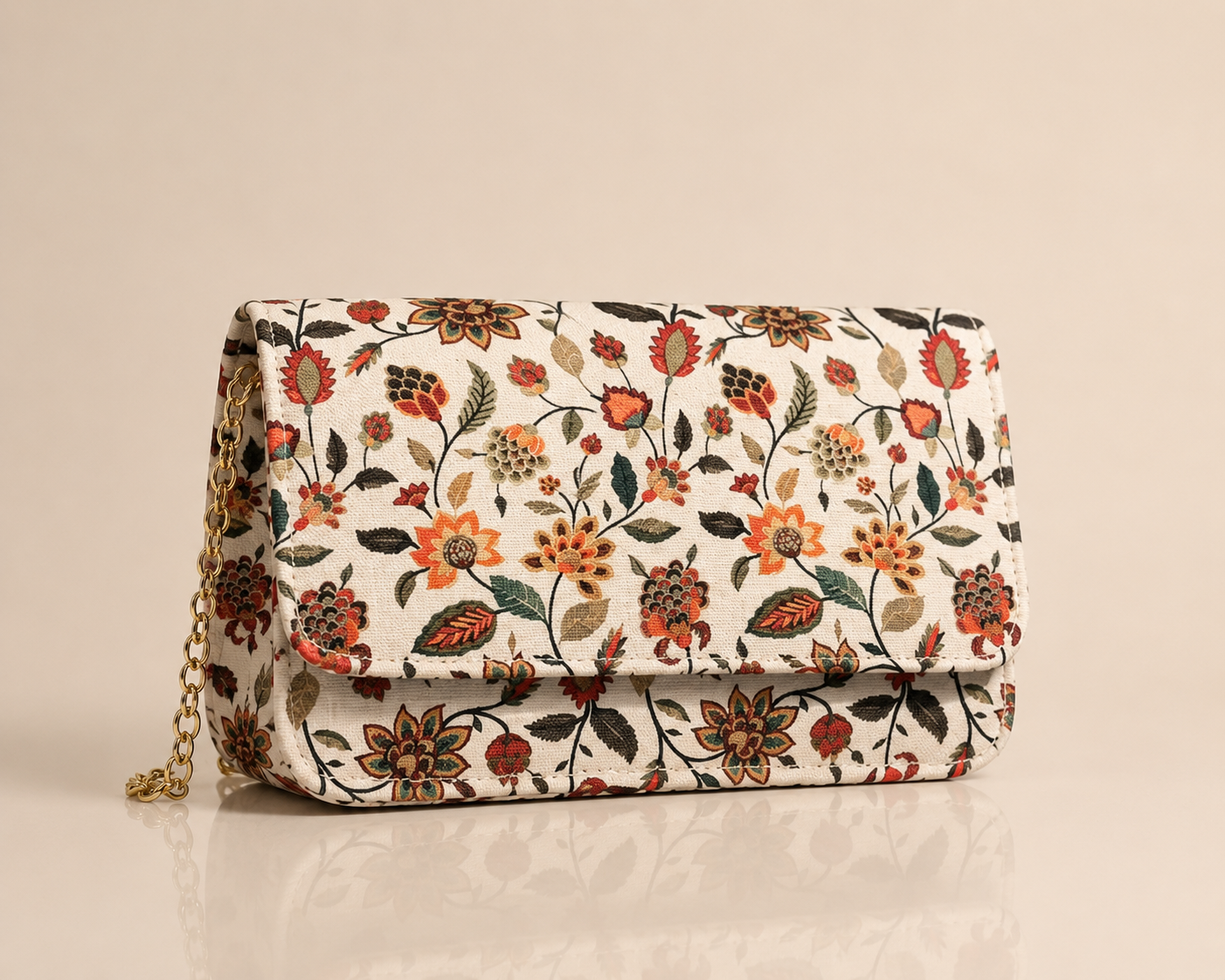 A rectangular clutch bag with a cream background and an all-over floral pattern in orange, red, green, and brown. It features a gold chain strap on the left side, set against a solid beige background with a soft reflection below.